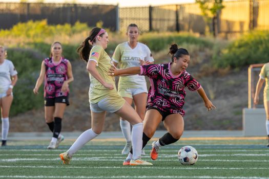 Action-packed photo of women playing an intense soccer match outdoors on a sunny day.