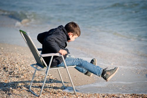 Boy Sitting on Chair Beside Seashore