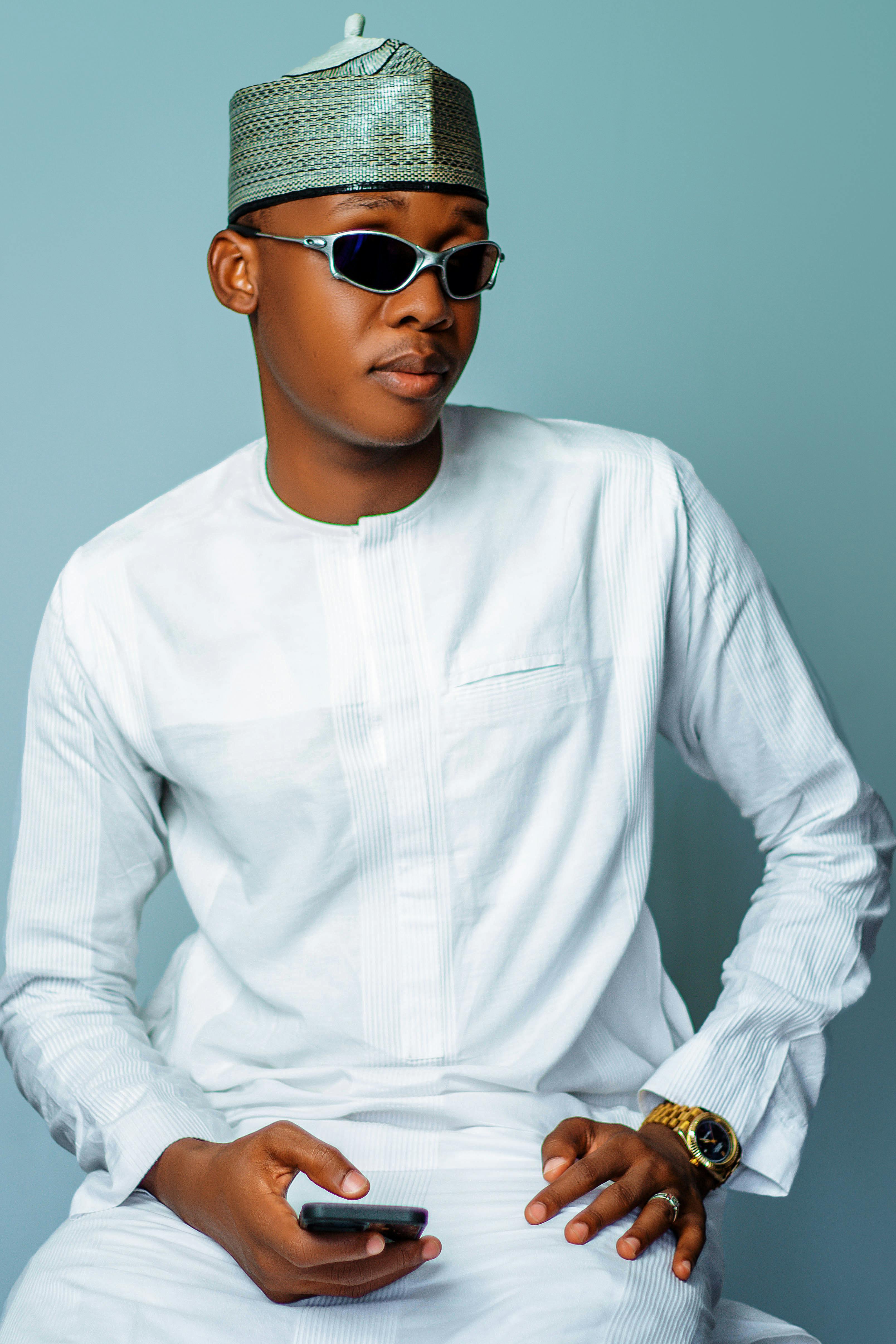 Stylish young man in white traditional dress and sunglasses holding a phone.