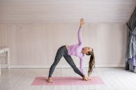 一名女子在室内的粉色垫子上练习瑜伽，展示出平衡与灵活性