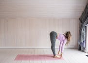 一位留着长发绺的女子在室内的粉红色垫子上做着前屈瑜伽姿势