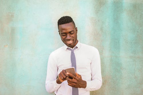 Man in White Dress Shirt Holding Black Smartphone Smiling