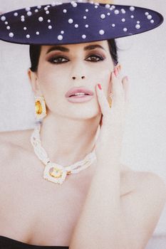 Portrait of a stylish woman wearing a pearl-studded hat and luxurious jewelry.