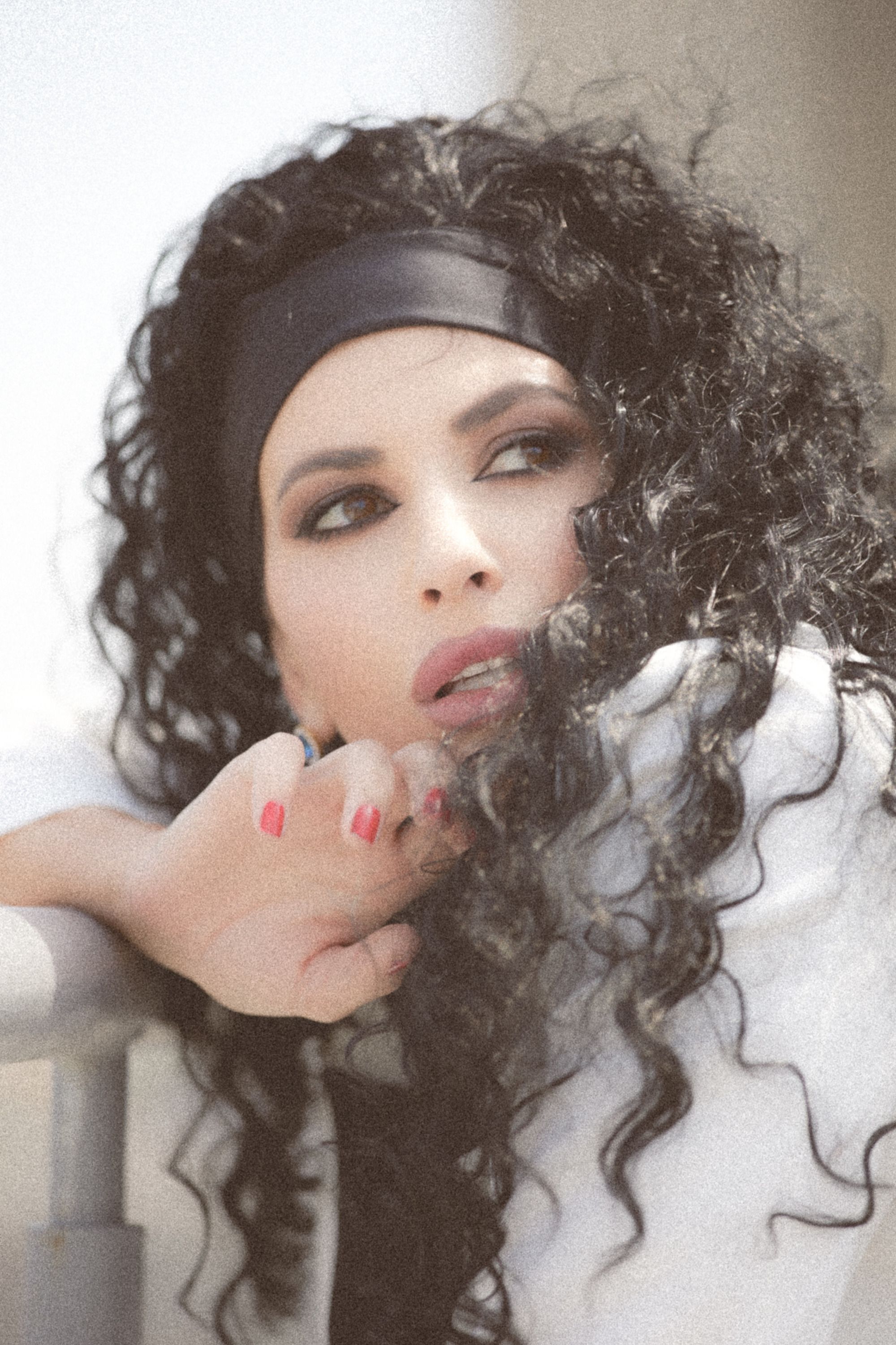 Stylish portrait of a woman with curly hair and makeup, wearing a headband, looking thoughtfully into the distance.