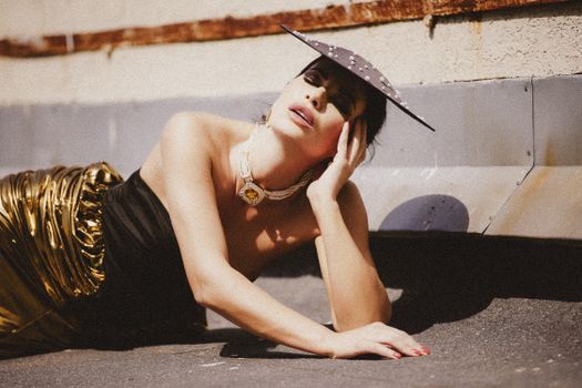 Stylish woman in a gold skirt and black top poses on an outdoor urban setting.