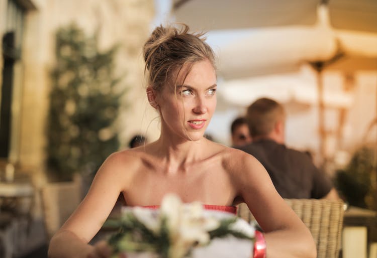 Selective Focus Photo Of Woman In Red Tube Top  Sitting Alone At A Table Looking Away