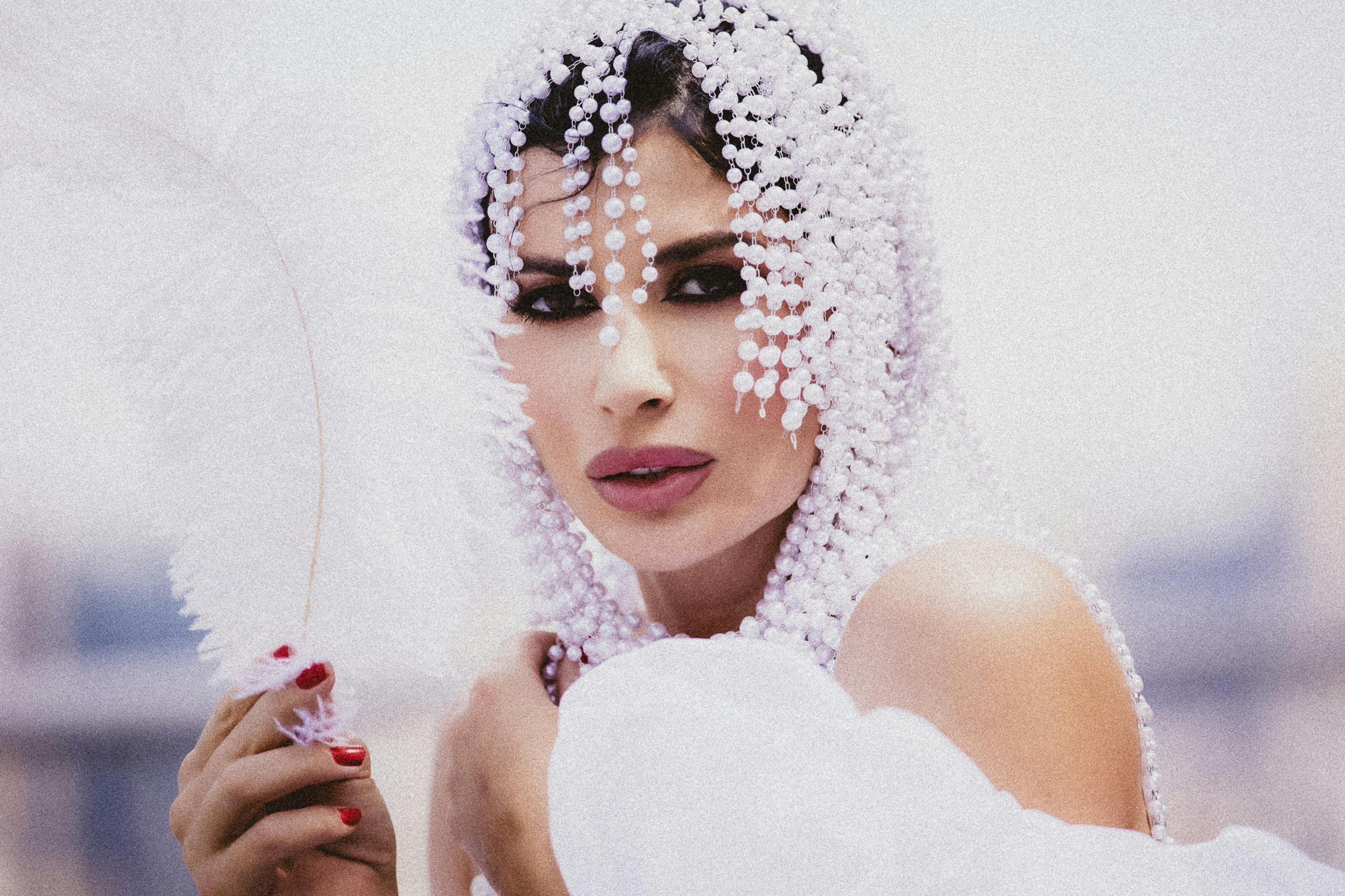 Elegant woman adorned in pearls holds a white feather, embodying grace and sophistication.