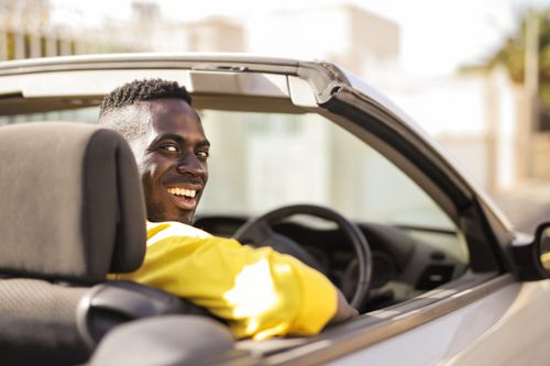 Free A man in a yellow shirt enjoys a sunny day while driving a convertible car. Stock Photo