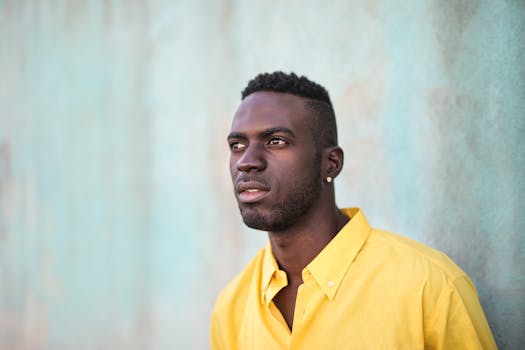 一位穿着黄色衬衫的时尚年轻人在户外对着纹理墙摆姿势