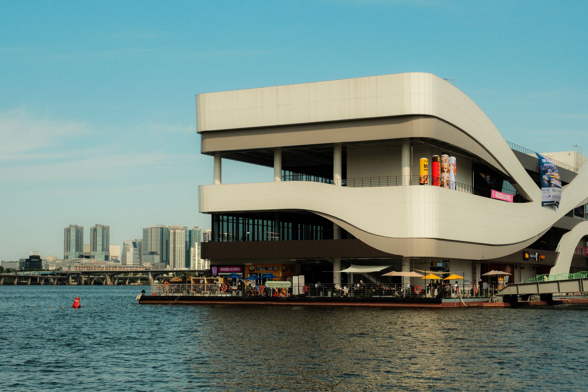 A modern building by the waterfront with a city skyline in the background, showcasing urban architecture.