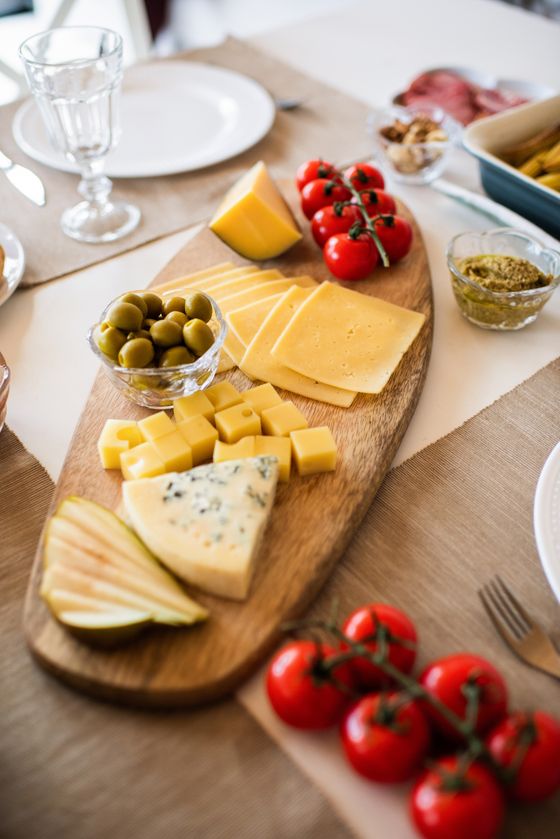 Wooden board with sliced yellow cheese, cheese cubes, blue cheese wedge, pear slices, olives and tomatoes