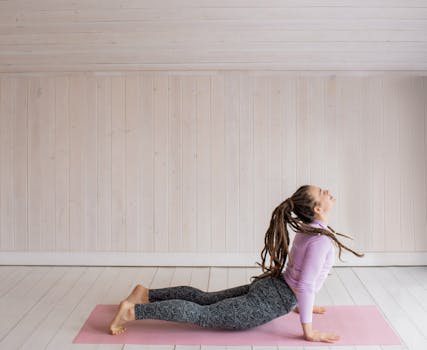 Woman with dreadlocks performing yoga pose on pink mat in a serene indoor setting.