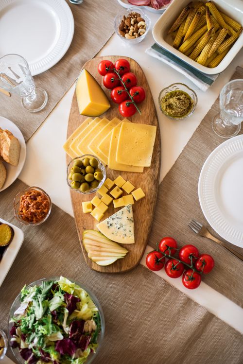 Free A delectable cheese platter with a variety of cheeses, fresh tomatoes, and olives on a wooden board. Stock Photo