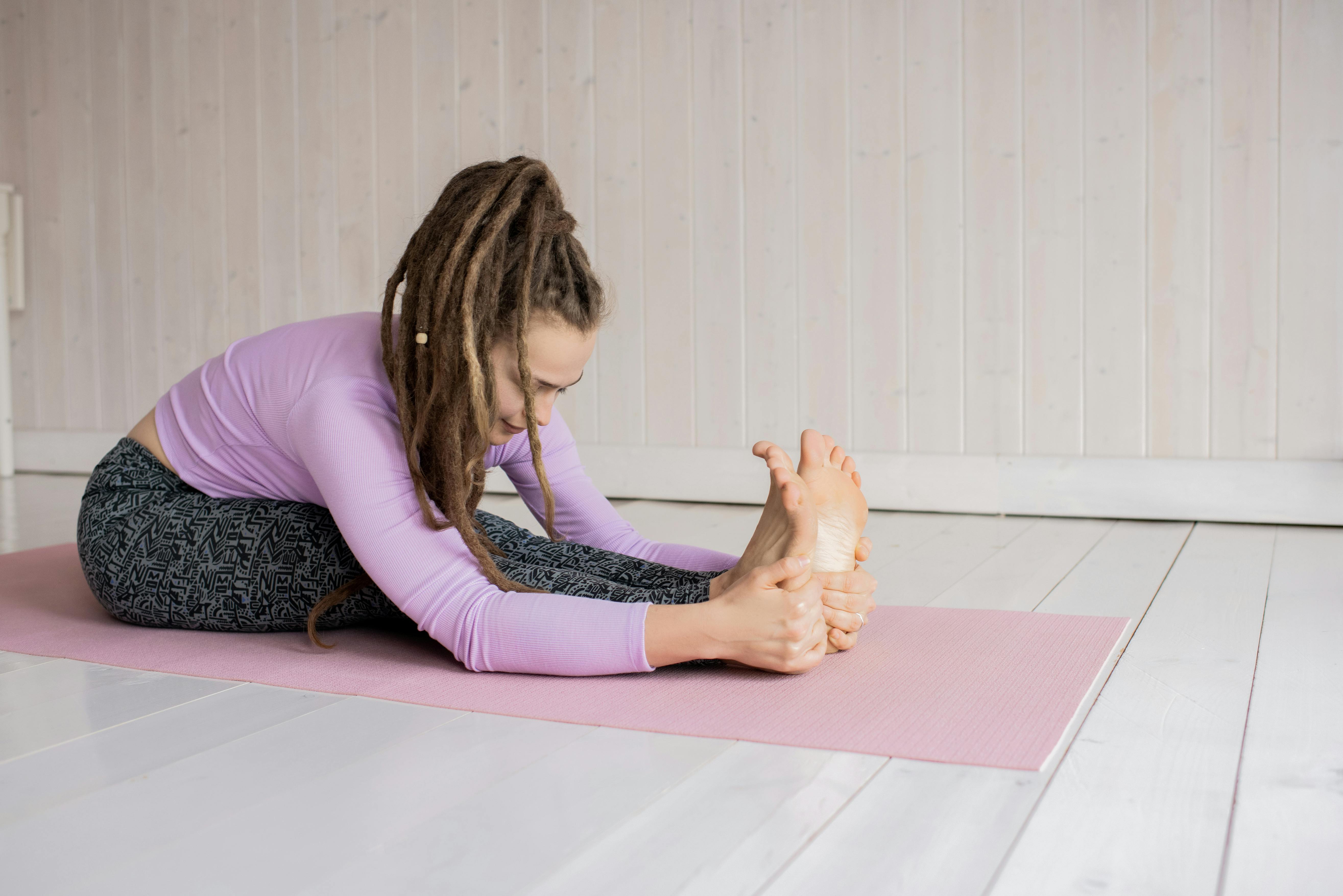 Free A woman stretching in a seated forward bend yoga pose on a pink mat indoors. Stock Photo