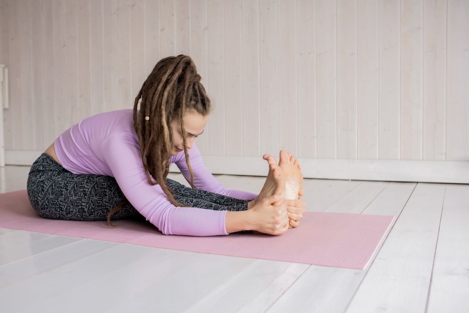 Woman practicing paschimottanasana seated forward bend yoga pose on a mat indoors