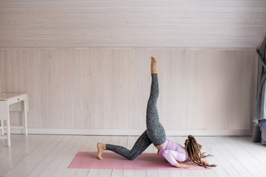 Woman practicing yoga indoors on a pink mat in a serene setting, showcasing flexibility and balance.