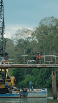 Workers on a bridge over a river amid lush trees, showcasing industry and nature.