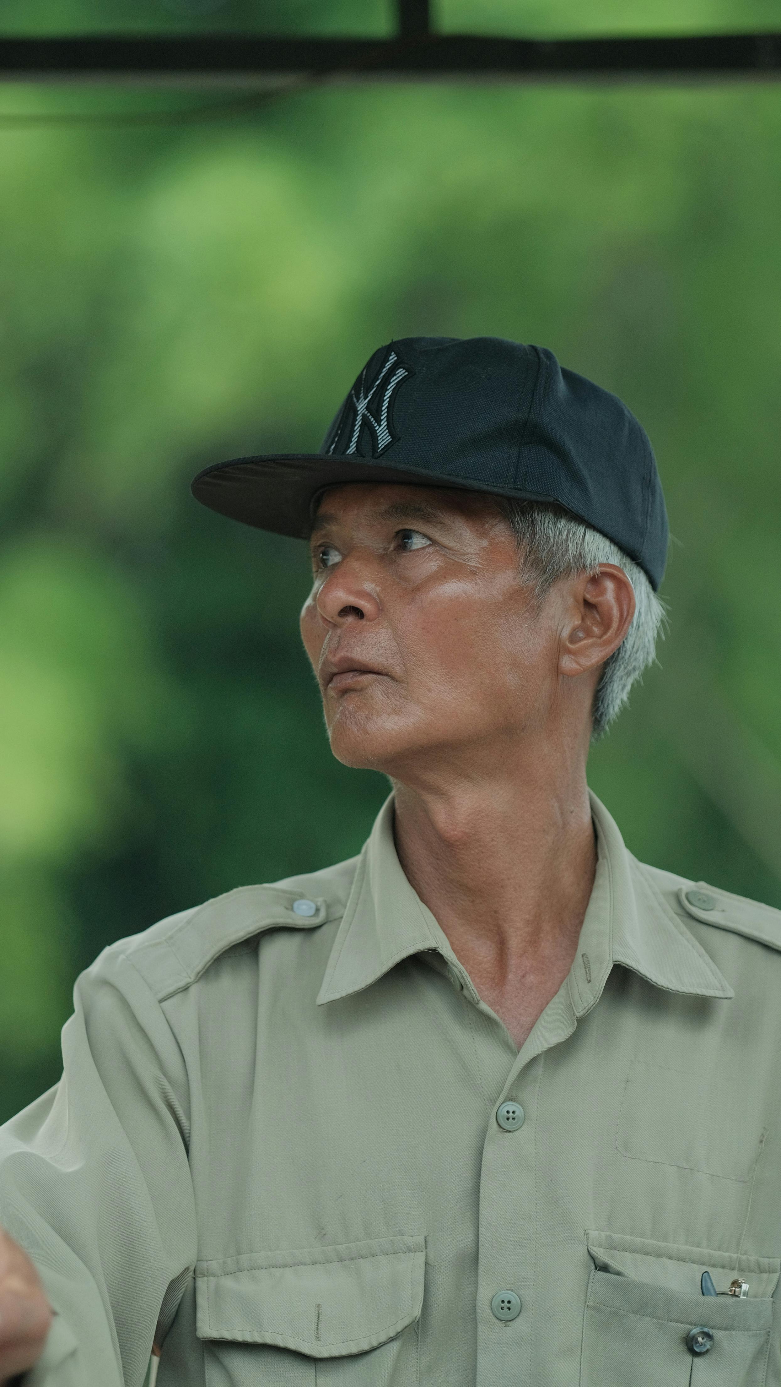 Elderly man wearing a cap looking contemplatively to the side in a natural outdoor setting.