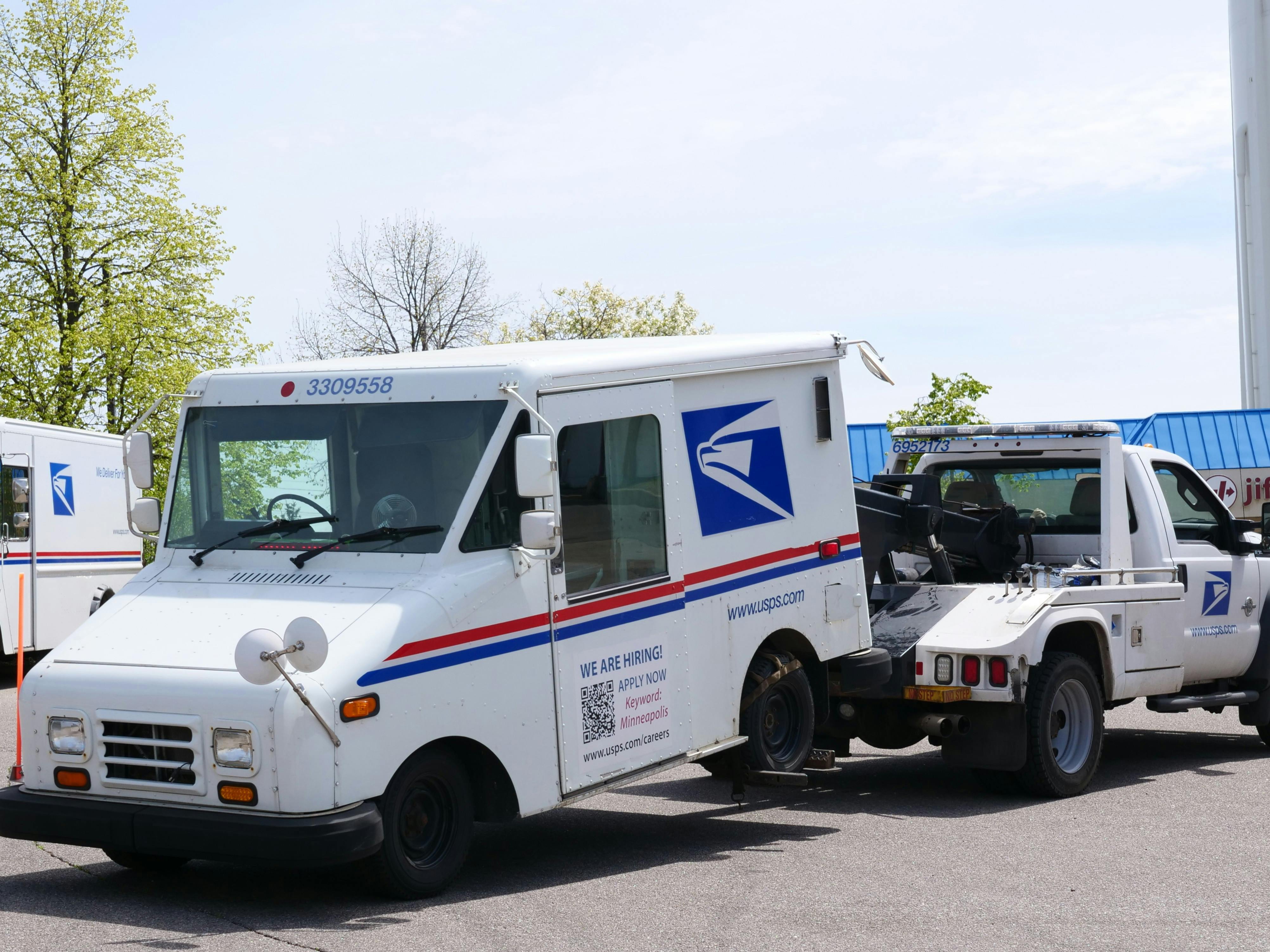 A United States Postal Service (USPS) mail truck is being towed outdoors on a clear day.