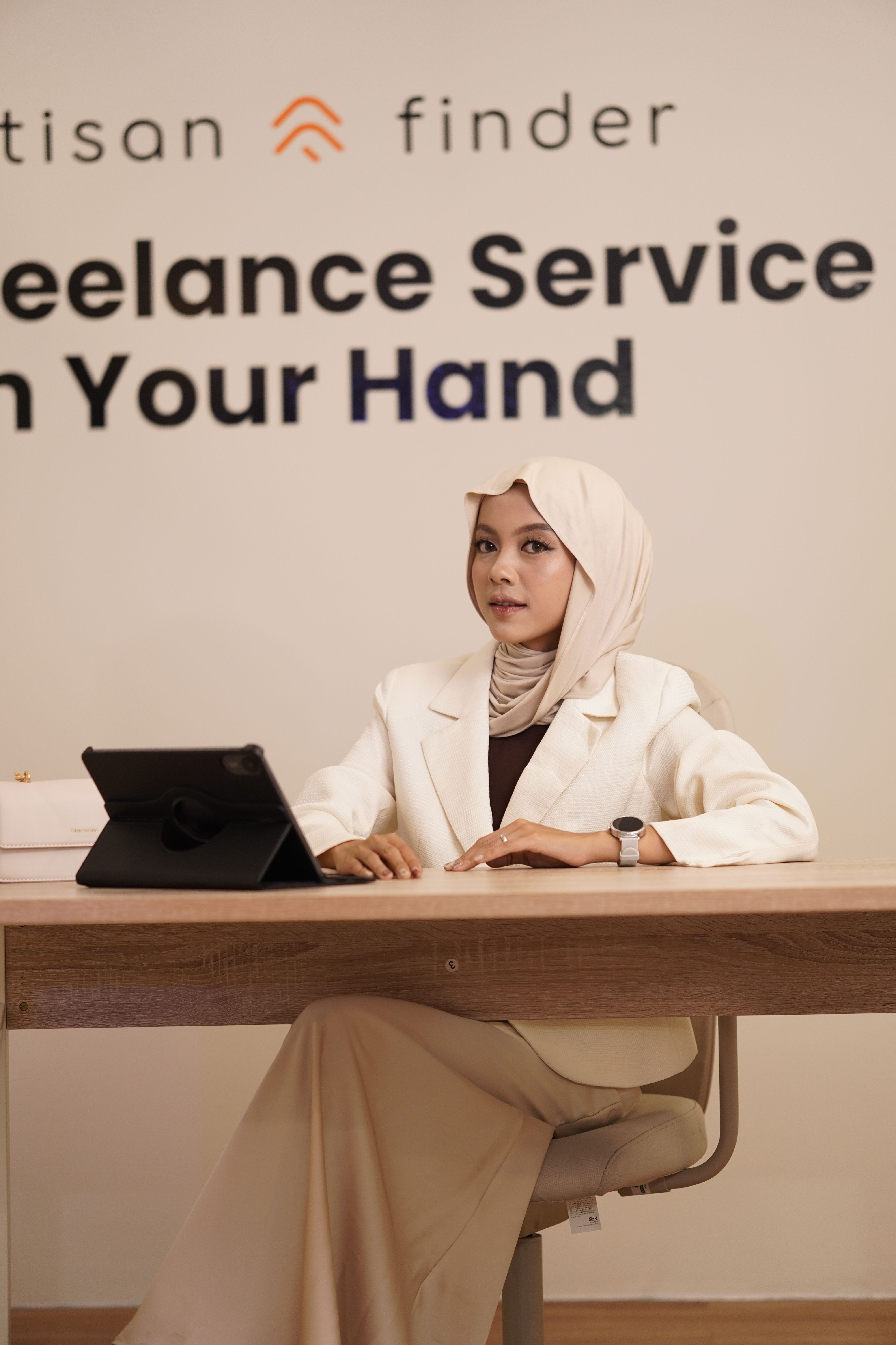 A woman in business attire sits at a desk with a digital tablet and promotional text in the background.