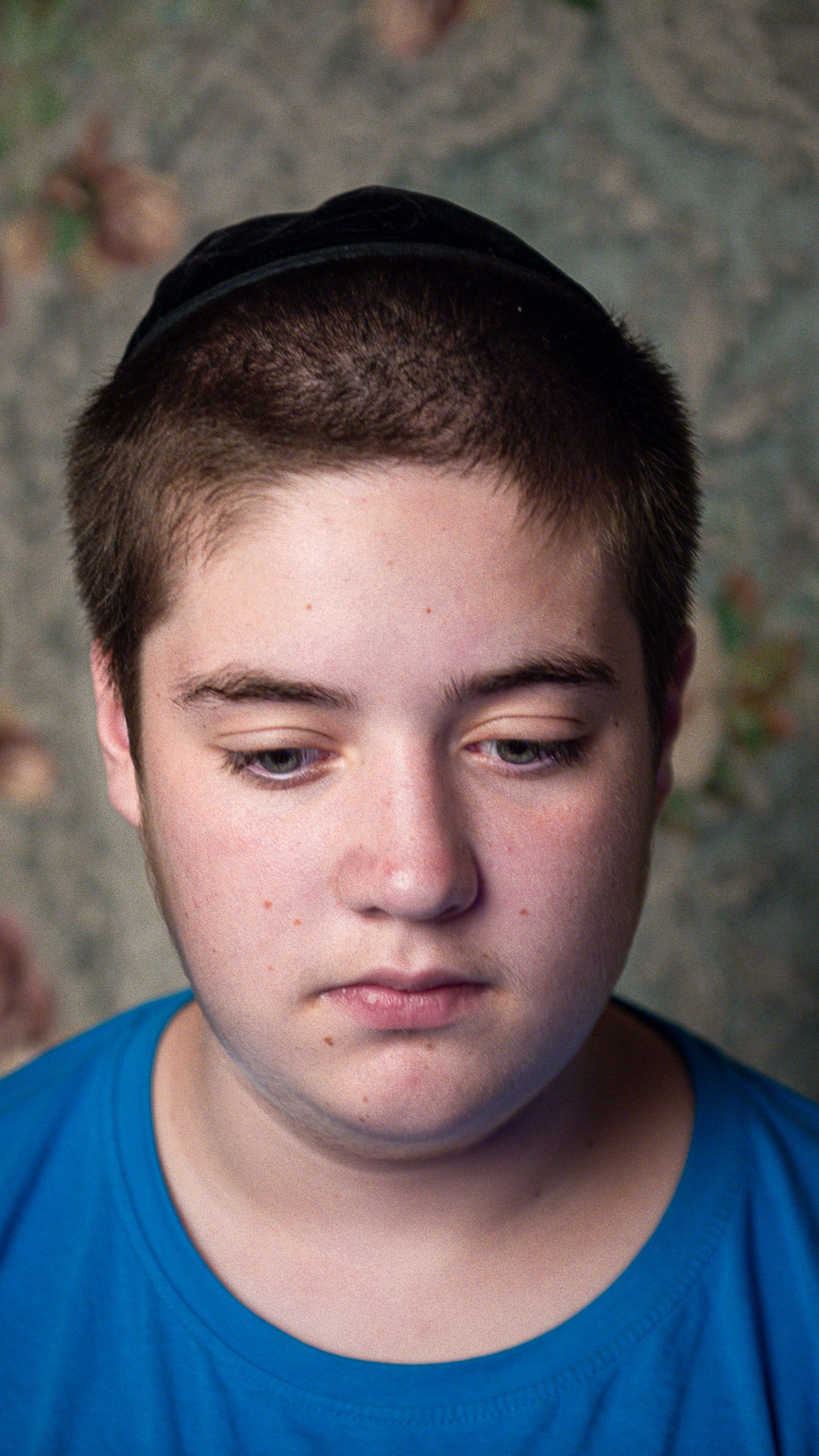 Portrait of a young teenager in a blue shirt looking thoughtful indoors with a decorative background.