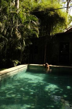 A person relaxing in an outdoor pool surrounded by lush tropical greenery.