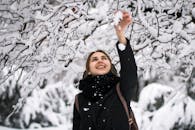 一个快乐的女人热情地微笑着，伸手去拿冬日仙境里树枝上的雪