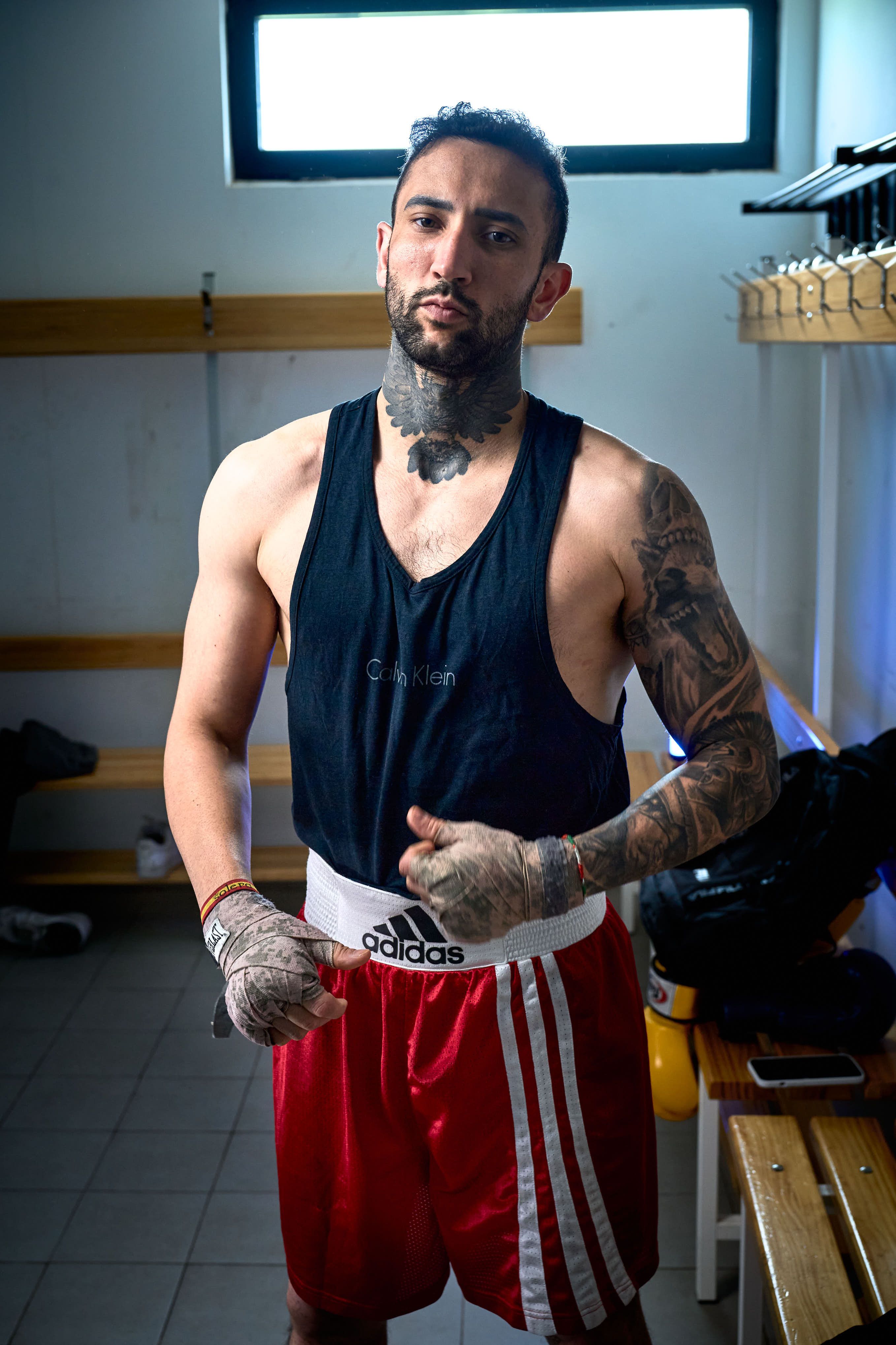 Tattooed male boxer prepares for a match in a Valladolid locker room, showcasing determination and athleticism.