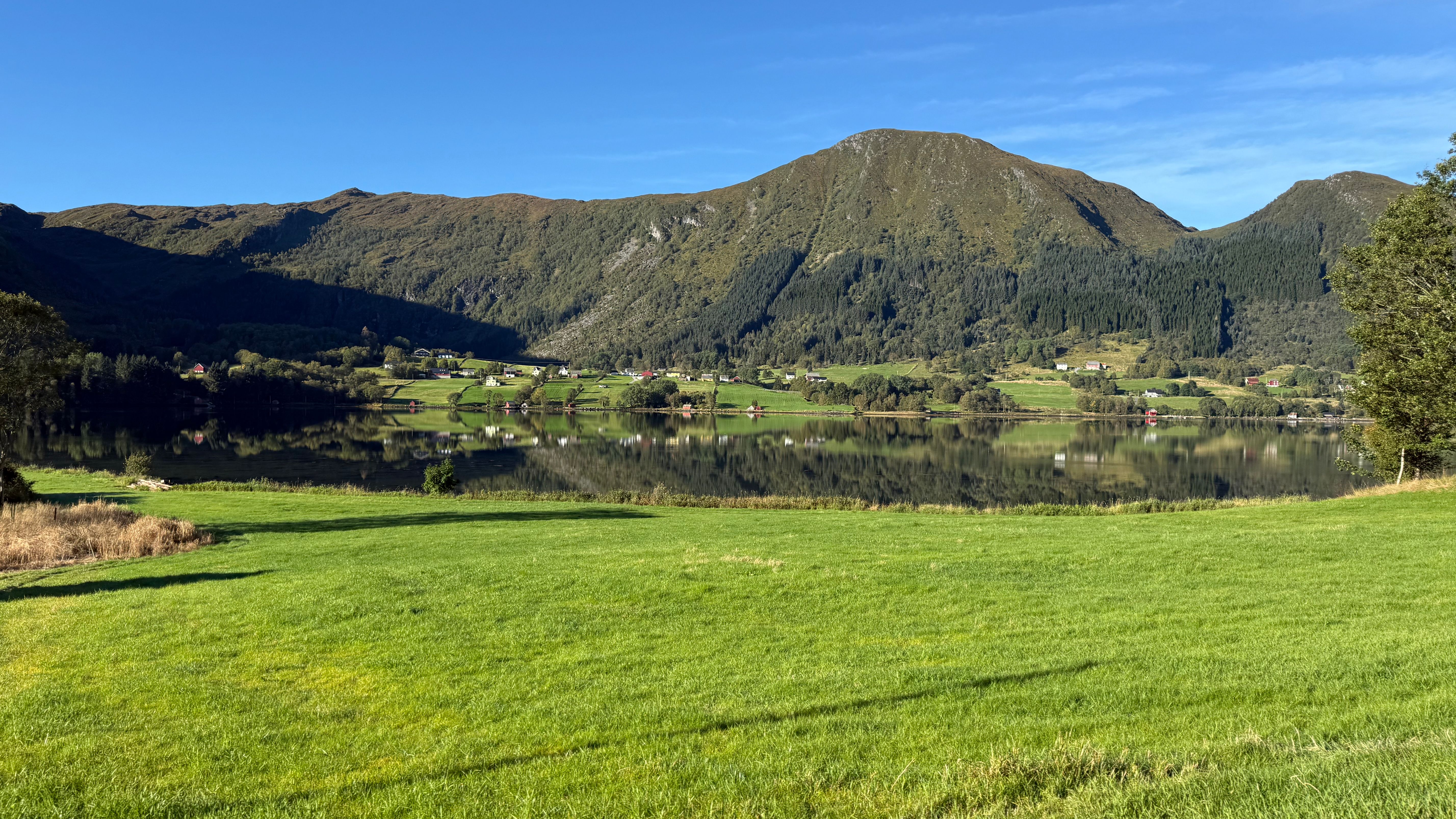 Gratis Fredelig fjellandskapsrefleksjon i en rolig innsjø under en klar blå himmel i Norge. Arkivbilde