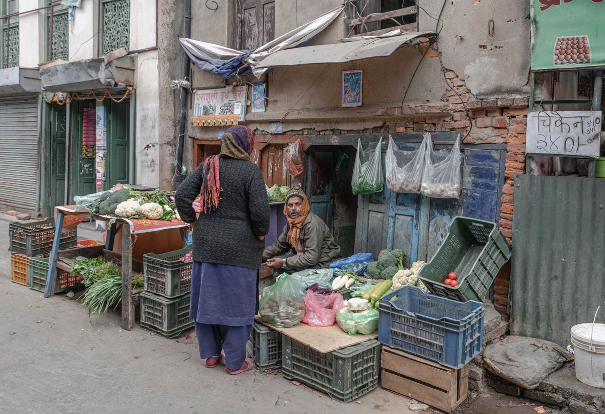 A woman buying greens at a small street vegetable stall in Kathmandu, crates stacked along the pavement