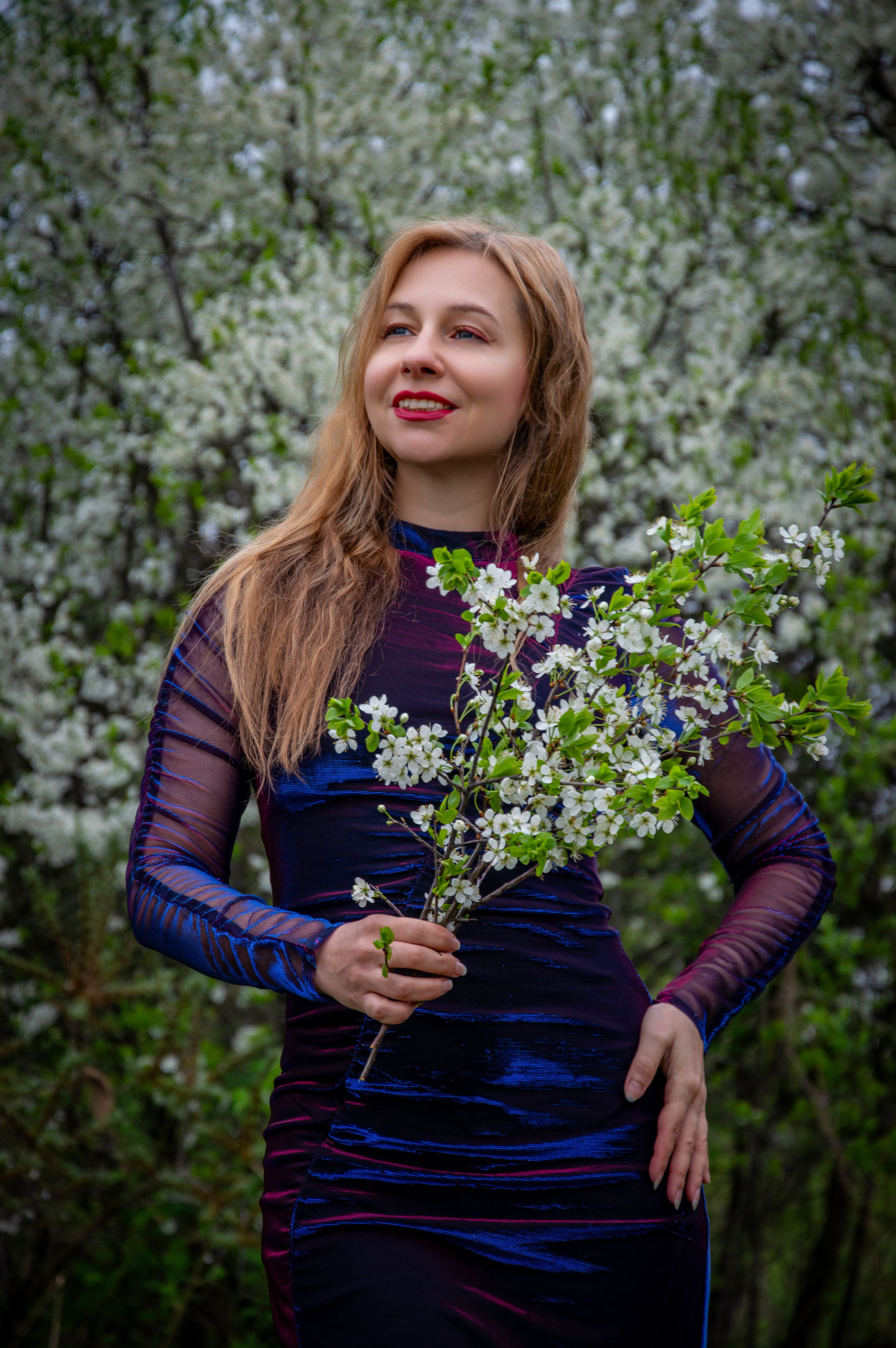 Smiling woman holding a bouquet of spring blossoms in a blooming garden.