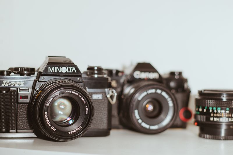 Classic Minolta and Canon analog cameras with a vintage lens on white background.