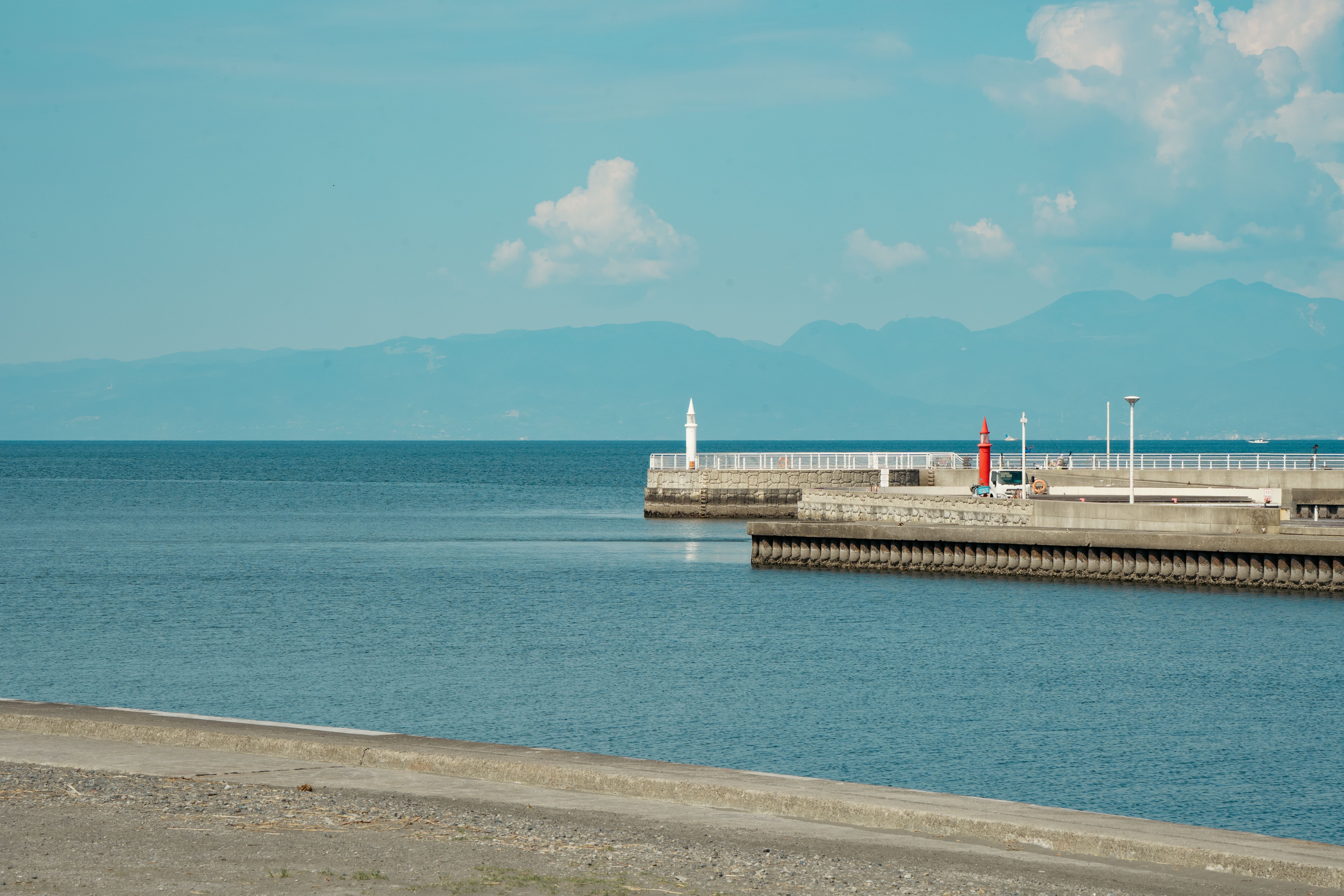 Tranquil view of Fujisawa harbor with distant mountains under a clear blue sky.