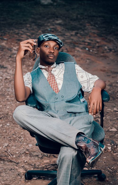 Free Young man in vintage suit and hat sitting leisurely outdoors, exuding style and confidence. Stock Photo