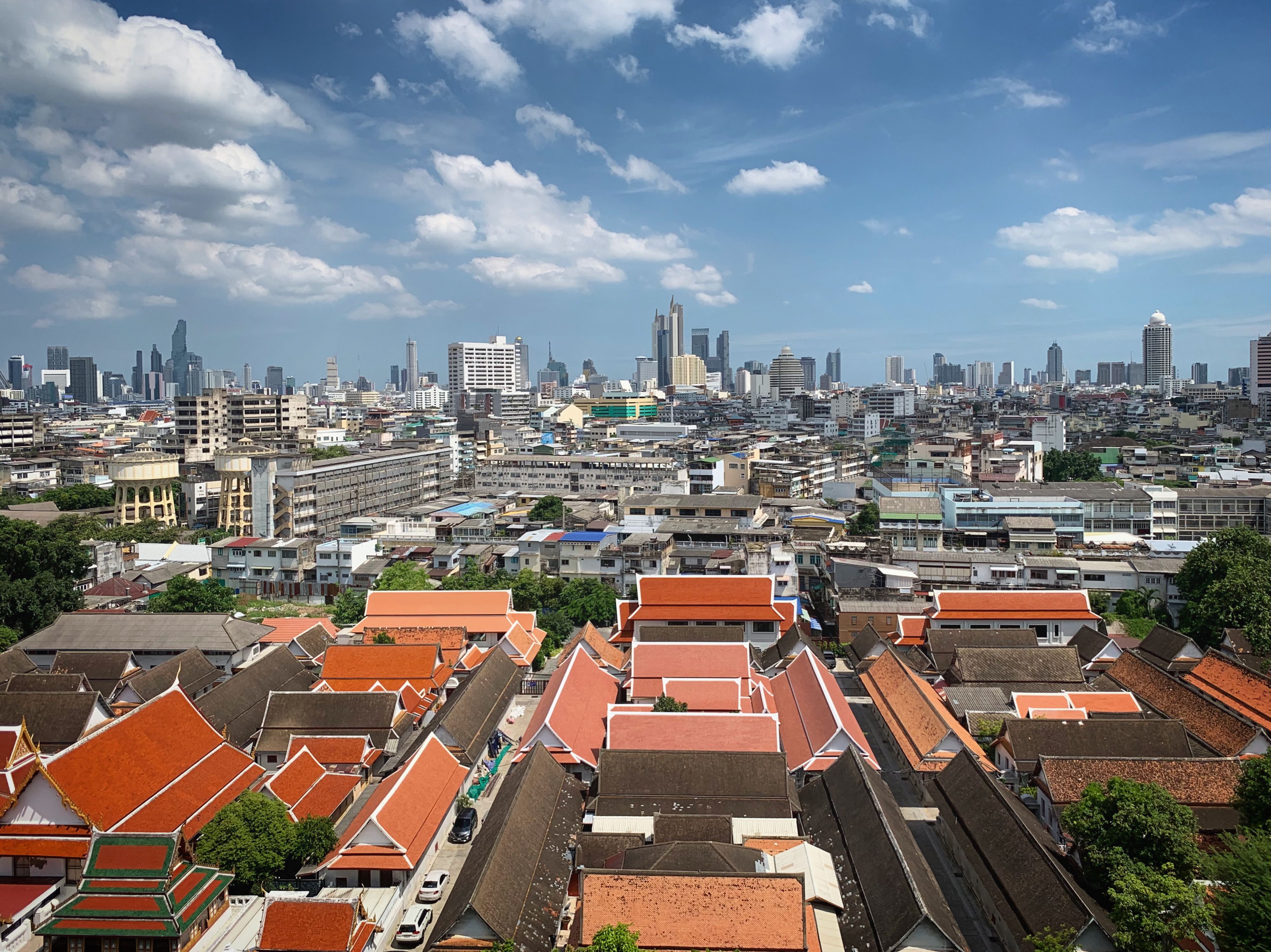 Aerial shot of Bangkok showcasing traditional Thai temples and modern skyline under a bright blue sky.