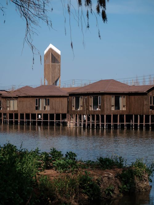 Free Lakeside wooden houses on stilts with a modern tower in the distance under a clear blue sky. Stock Photo