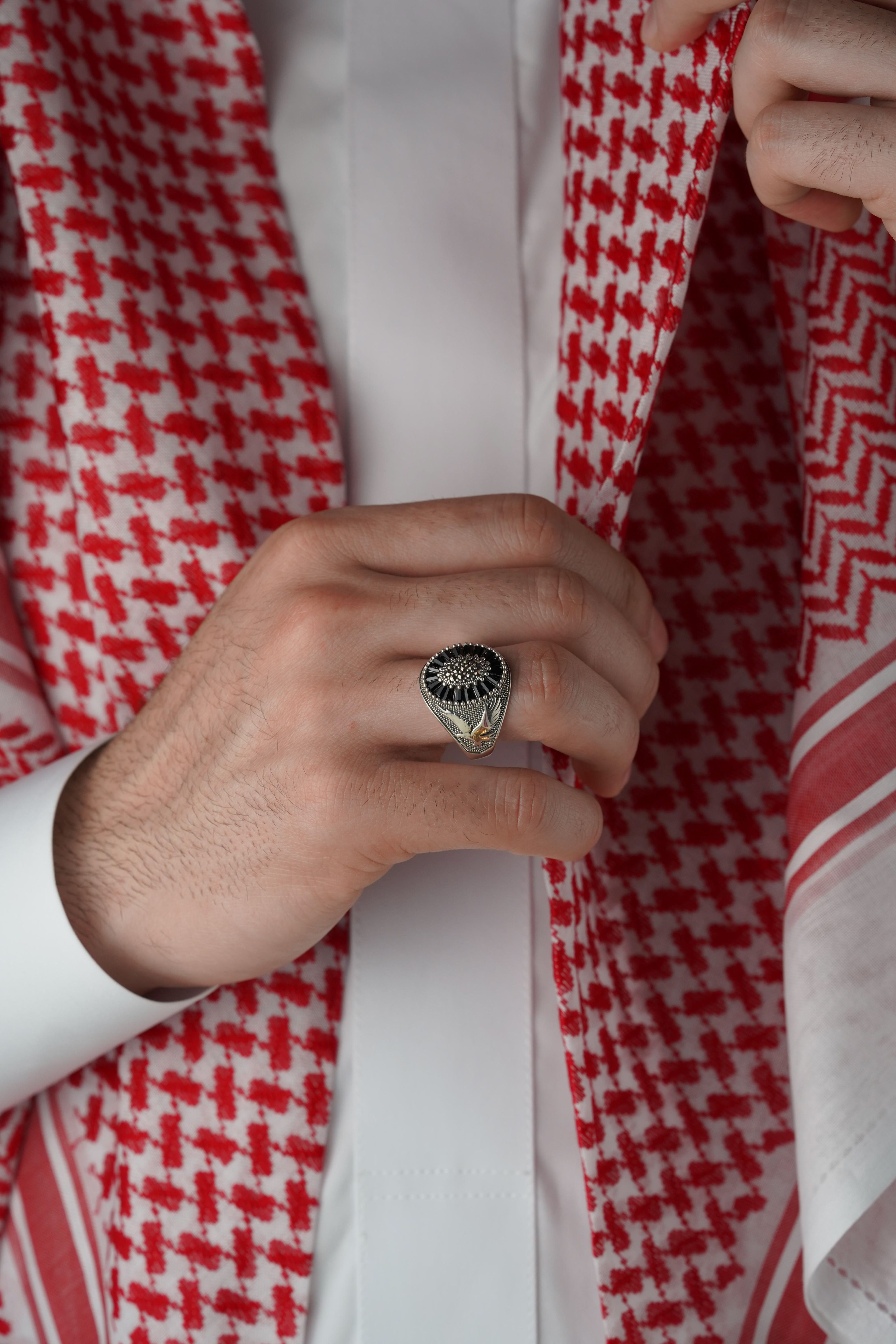 Close-up of a luxury men's ring complemented by traditional Middle Eastern attire and red keffiyeh.