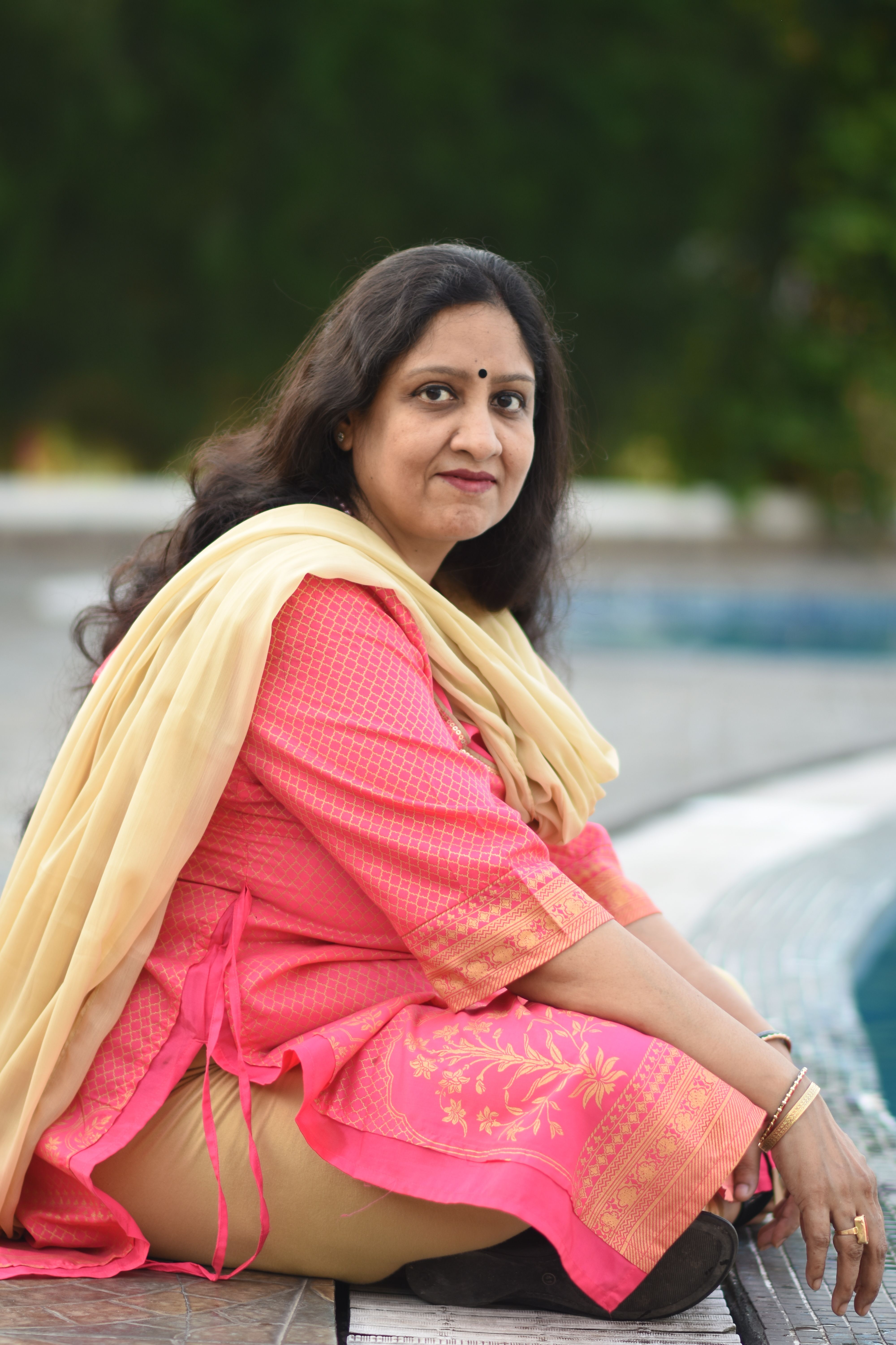 Portrait of an Indian woman sitting by a pool, dressed in traditional attire, outdoors.
