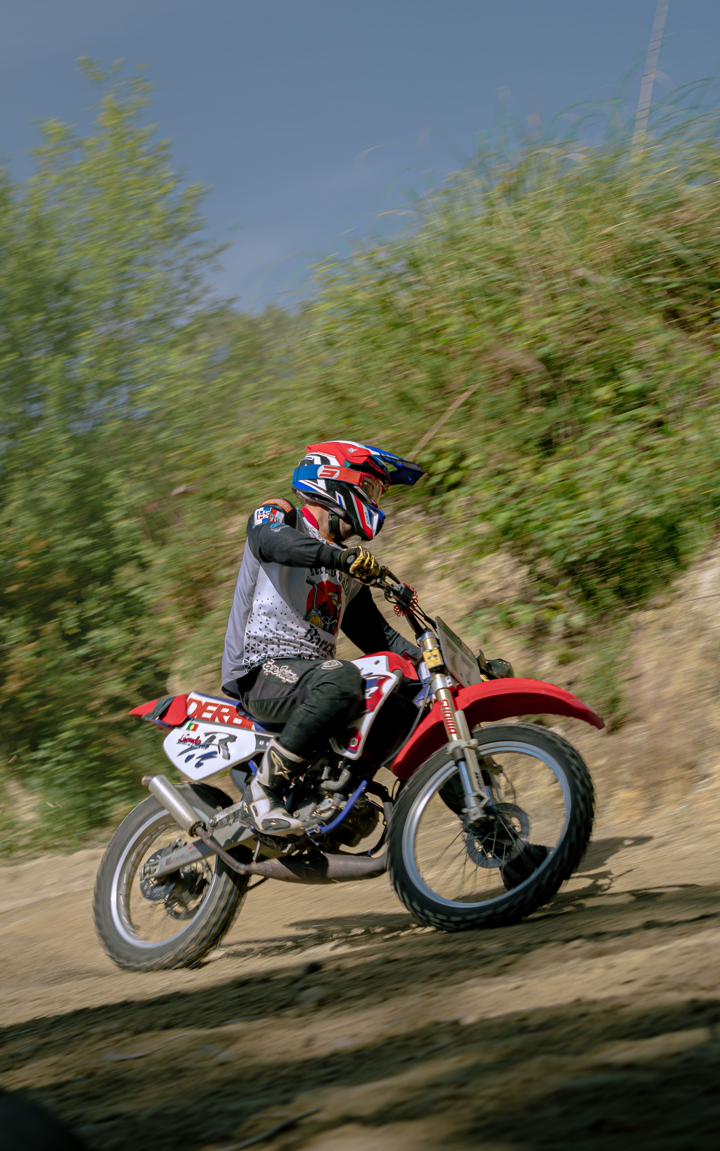 Dynamic shot of a motocross rider on a dirt trail with mud splashes and greenery.