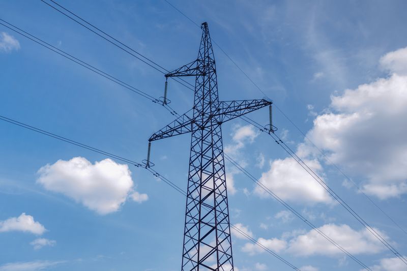 A high voltage transmission tower set against a bright blue sky with scattered clouds, showcasing modern infrastructure.