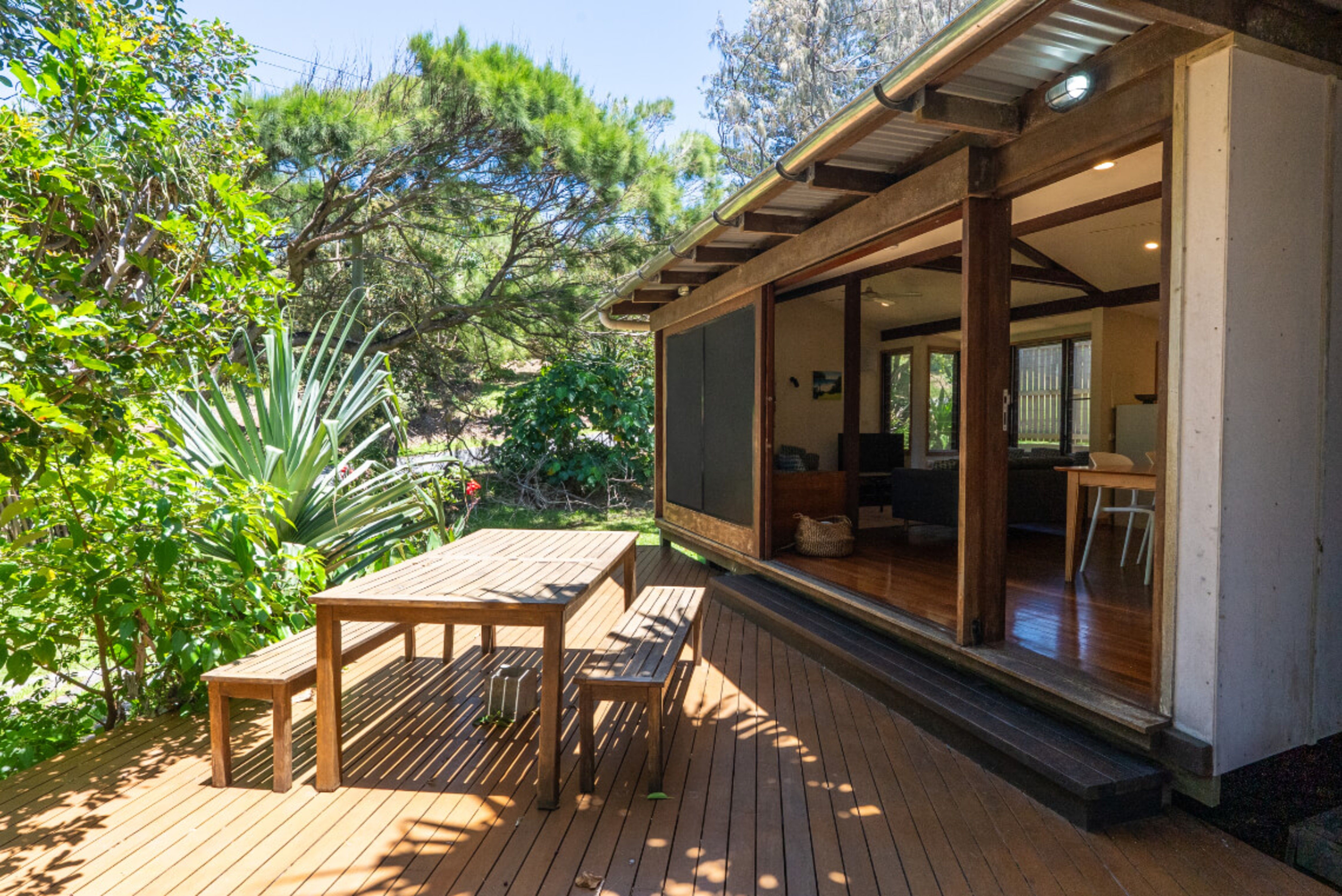 A modern outdoor patio with wooden deck, furniture, and open sliding doors to a home.