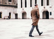 一名男子穿着外套，走过现代城市广场，展示着城市建筑