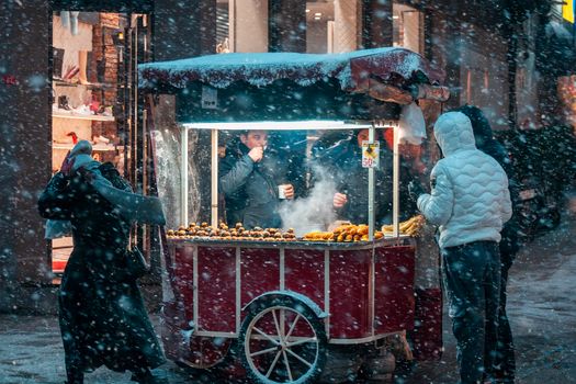 A street vendor selling snacks during a snowy night in the city.