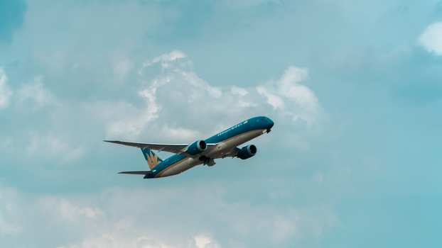 A commercial airplane flying through a cloudy blue sky, showcasing aviation travel.