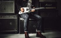 Man Sitting on Guitar Amplifier Playing Electric Guitar