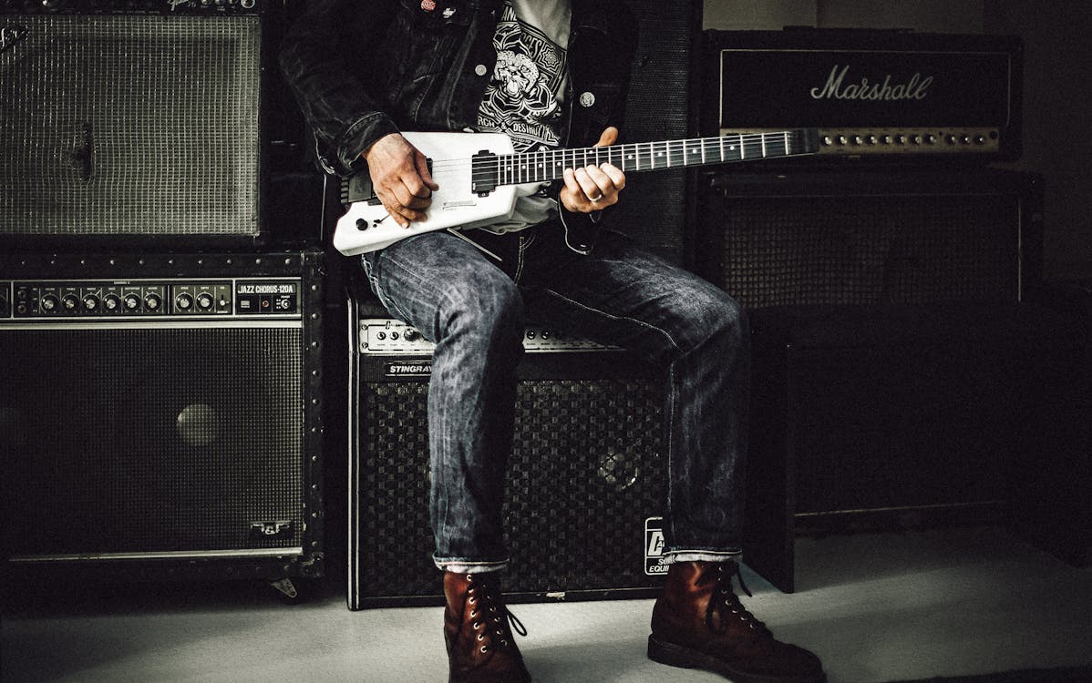 Man Sitting on Guitar Amplifier Playing Electric Guitar