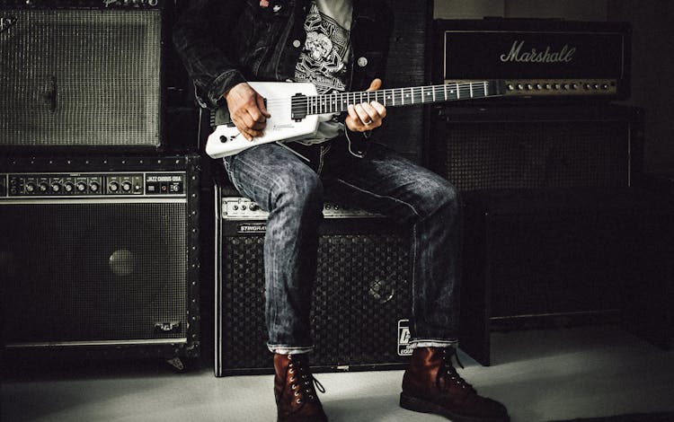 Man Sitting On Guitar Amplifier Playing Electric Guitar