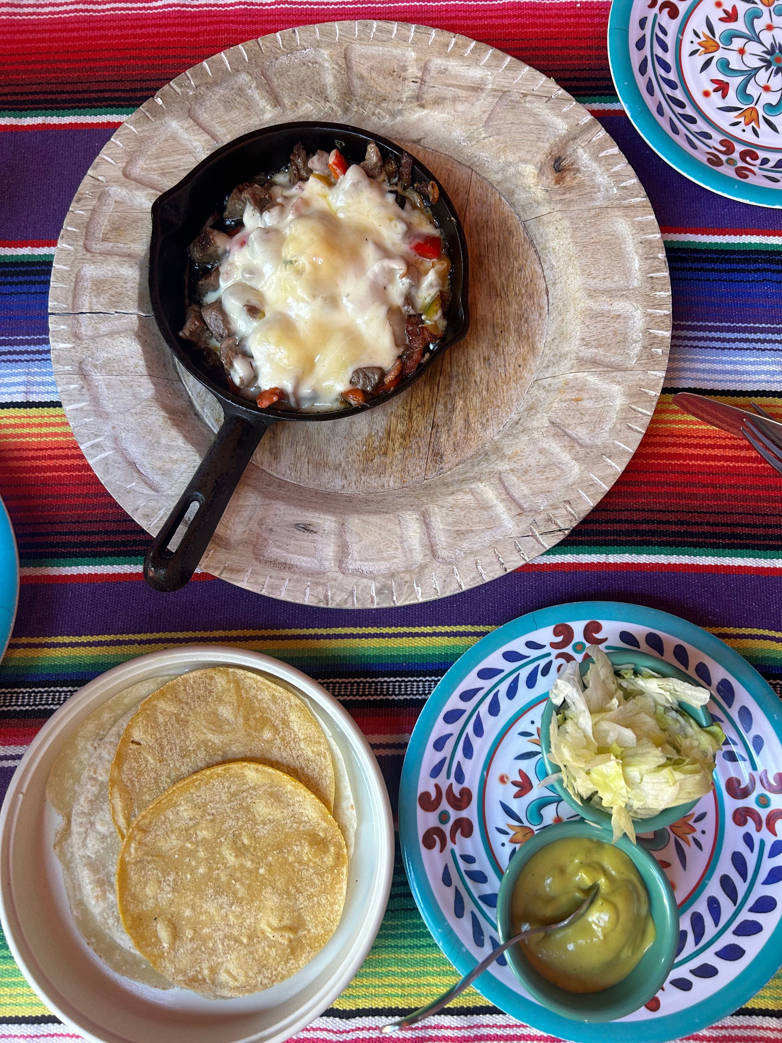 A cast iron skillet of Mexican chicken and rice with black beans, corn, and melted Monterey Jack cheese, topped with cilantro and lime wedges.