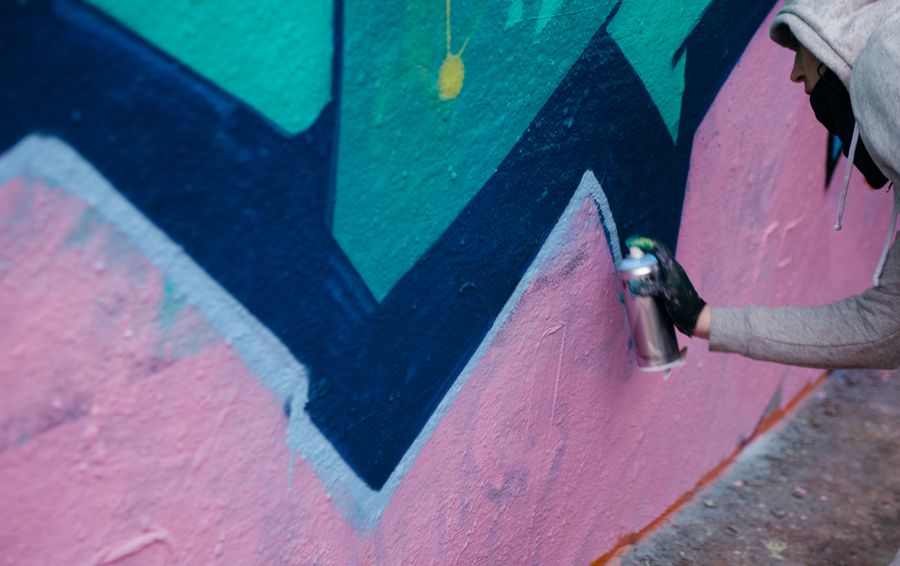 Artist spray painting angular blue and pink shapes on a wall