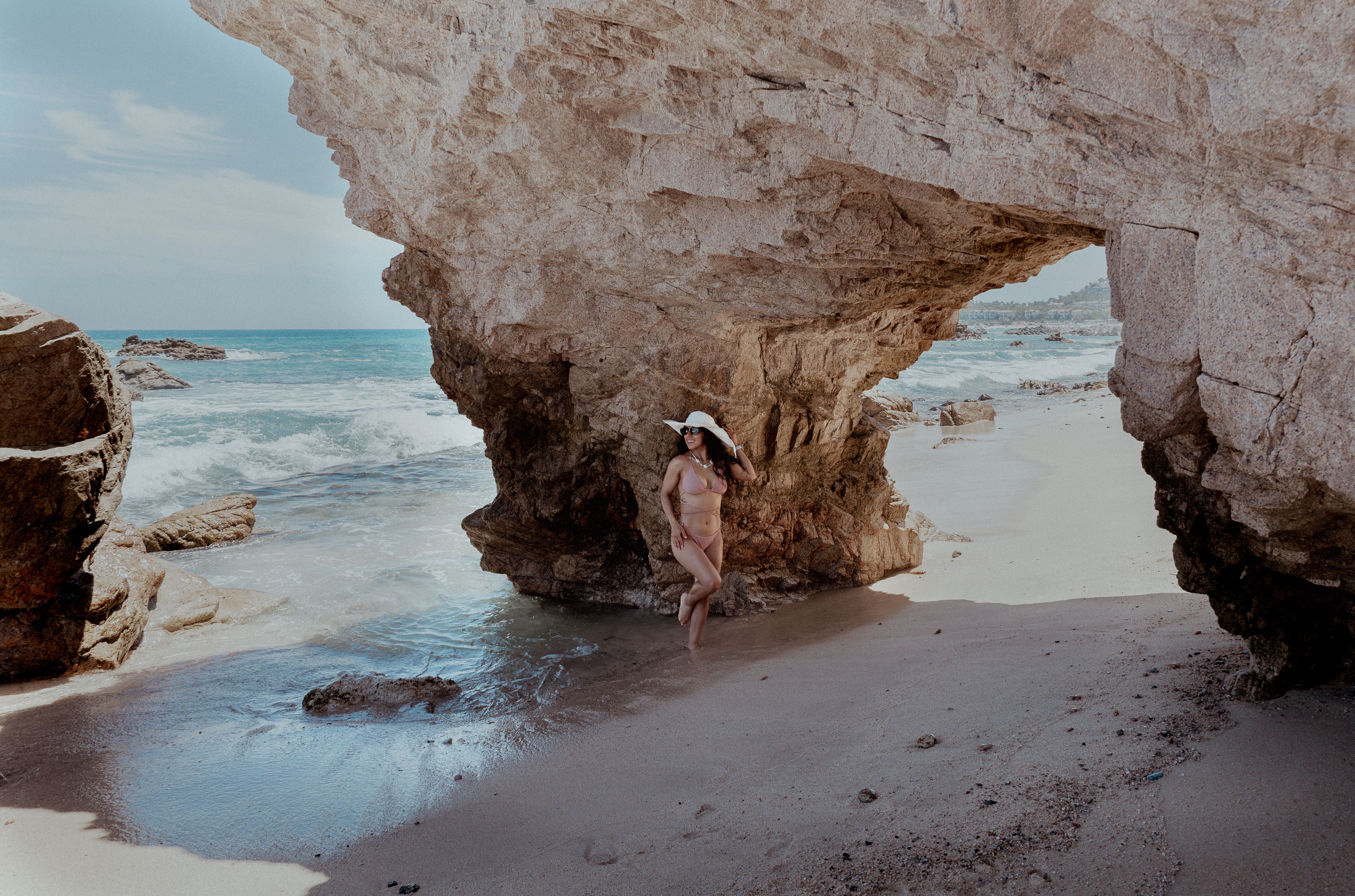 Free A woman in a bikini stands beneath a natural rock arch by the ocean in Cabo San Lucas. Stock Photo